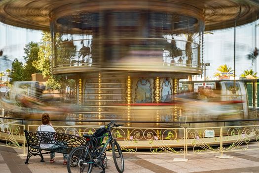 Fuengirola, Spain - June 31, 2018. the moving carousel and the woman sitting on the bench next to a bicycle