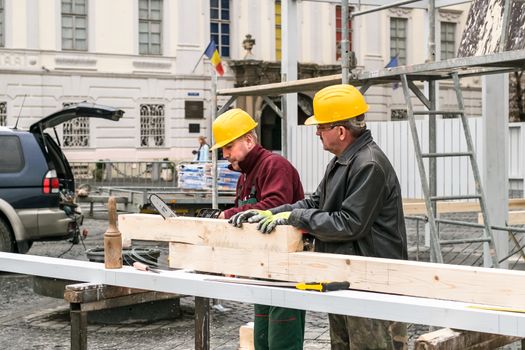 Sibiu, Romania - September 29, 2018. two workers cutting a beam for construction with a chainsaw in a grand square, Sibiu, Romania