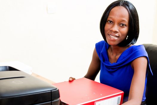 Young smiling secretary sitting at her desk and holding a binder