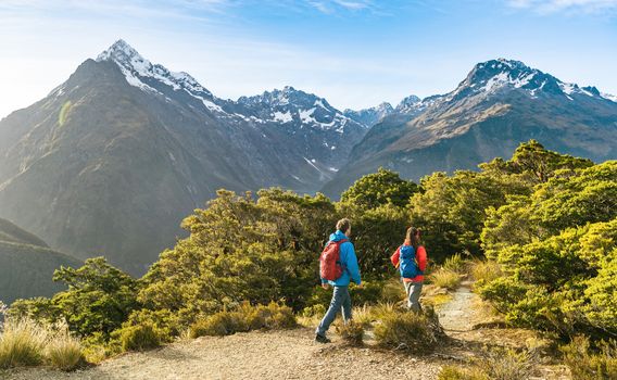 Hiking couple walking on trail at Routeburn Track in New Zealand. Hikers trekking wearing backpacks while tramping on Key Summit Track on vacation at Fiordland National Park, New Zealand.