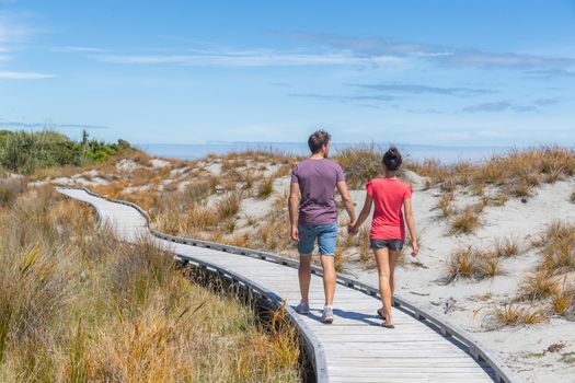 Couple walking on beach holding hands romantic in New Zealand - young people in Ship Creek on West Coast of New Zealand. Tourist couple sightseeing on South Island of New Zealand.