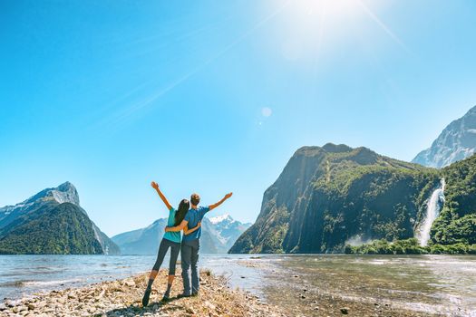 Outdoor couple happy with arms outstretched in Milford Sound New Zealand in nature enjoying active outdoor lifestyle hiking in Milford Sound, New Zealand by Mitre Peak in Fiordland.