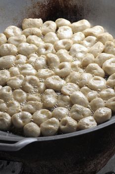 Many white fish balls are in a large iron pan, With boiling oil.
