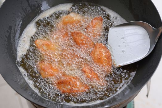 Chicken wings are frying in an iron pan with boiling oil.