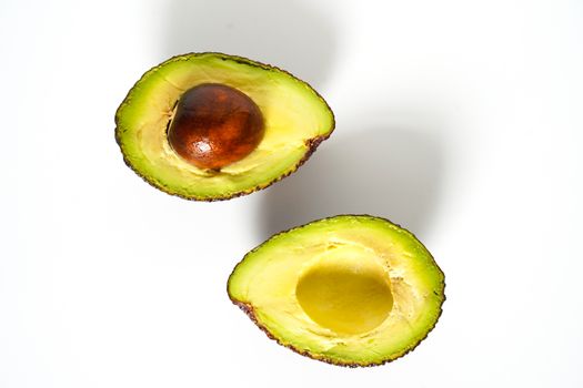 An avocado sliced in half to reveal the core against a plain whit background