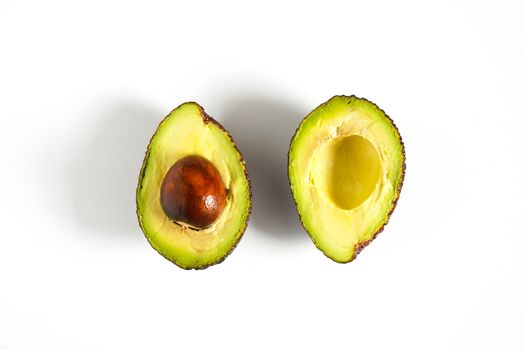 An avocado sliced in half to reveal the core against a plain whit background