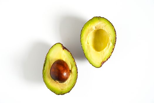 An avocado sliced in half to reveal the core against a plain whit background