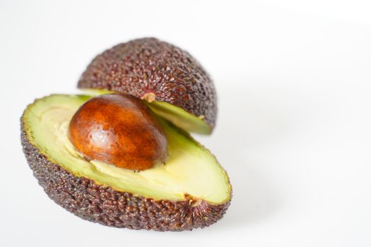 An avocado sliced in half to reveal the core against a plain whit background