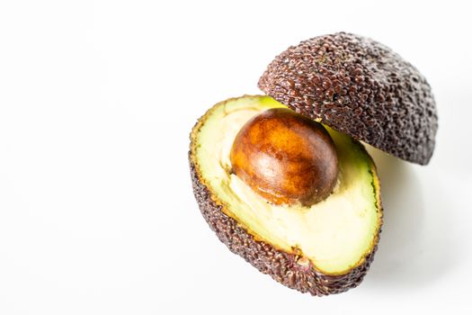 An avocado sliced in half to reveal the core against a plain whit background