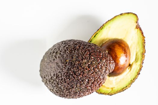 An avocado sliced in half to reveal the core against a plain whit background