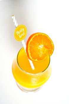 An orange cocktail drink with a party straw against a plain white background