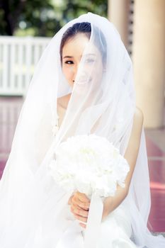 Portrait of a beautiful bride covering her face with a veil. Bright makeup with hand hold flower