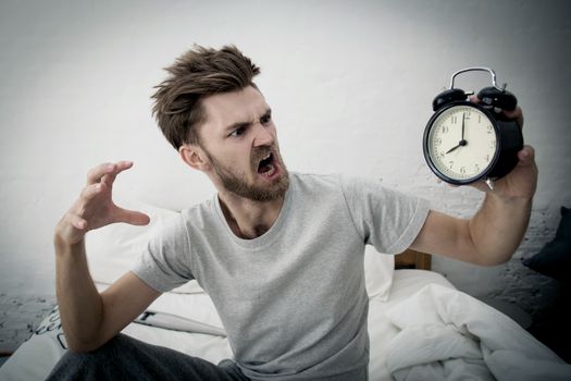 Portrait upset angry young man screaming at alarm clock on bedroom. Employee running late. Time management with business concept