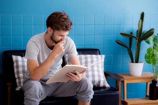Young man reading book on sofa in the living room