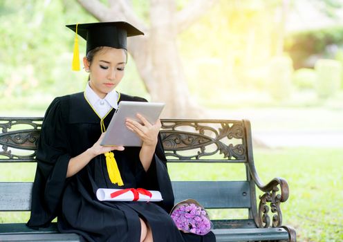 Graduate playing tablet in her hand feeling relaxing and so happiness in commencement day and search job new