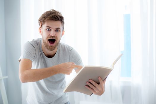 Handsome guy in eyeglasses is reading book preparing exam with standing at the living room - education concept.