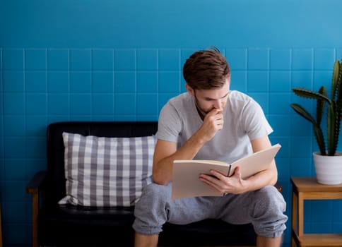 Young man reading book on sofa in the living room.
