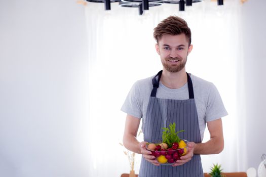 man is chef holding bowl with fruit with a smile in kitchen