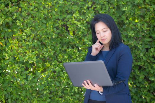 portrait of a businesswoman standing and using laptop on tree wall.