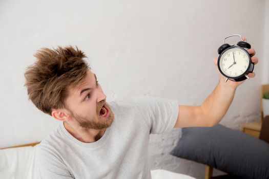 Portrait upset angry young man screaming at alarm clock on bedroom. Employee running late -  Time management with business concept.