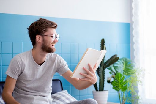Young man wear glasses reading book on sofa with enjoy and laugh in the living room with education concept.