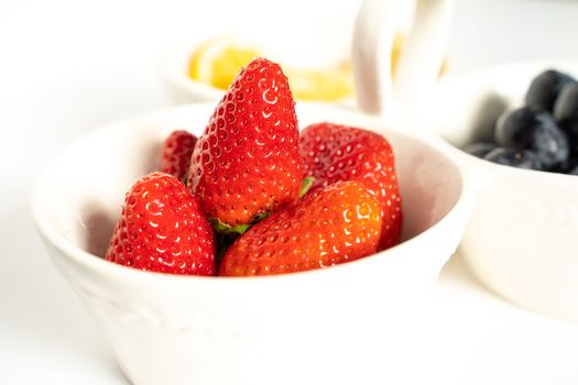 A serving dish filled with strawberries, lemon slices and black grapes against a plain white background