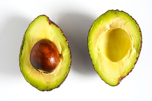 An avocado sliced in half to reveal the core against a plain whit background