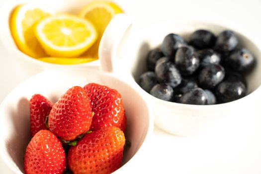 A serving dish filled with strawberries, lemon slices and black grapes against a plain white background