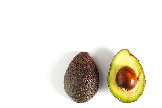 An avocado sliced in half to reveal the core against a plain whit background