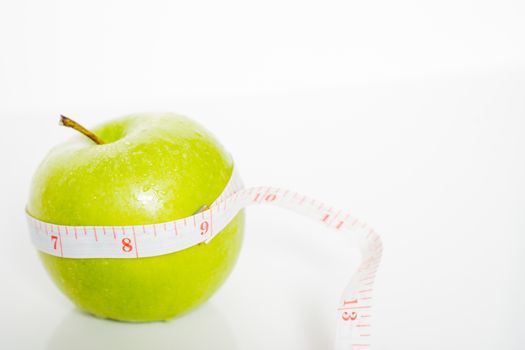A granny smith green apple with a measuring tape wrapped around it against a plain white background