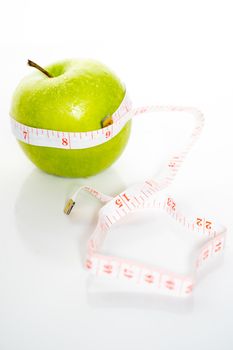 A granny smith green apple with a measuring tape wrapped around it against a plain white background