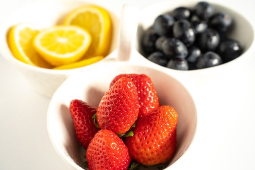 A serving dish filled with strawberries, lemon slices and black grapes against a plain white background