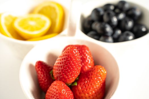 A serving dish filled with strawberries, lemon slices and black grapes against a plain white background