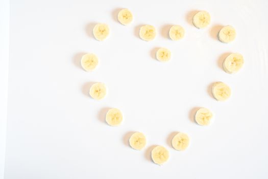 Slices of banana in the shape of a heart pattern against a plain white background