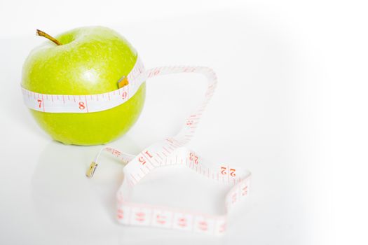 A granny smith green apple with a measuring tape wrapped around it against a plain white background