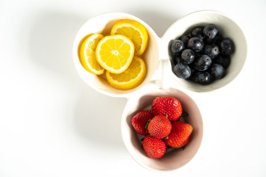 A serving dish filled with strawberries, lemon slices and black grapes against a plain white background