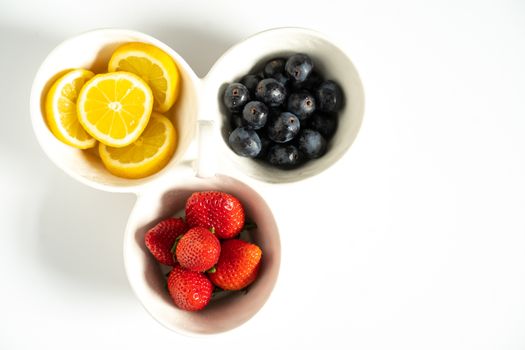 A serving dish filled with strawberries, lemon slices and black grapes against a plain white background