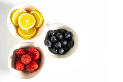 A serving dish filled with strawberries, lemon slices and black grapes against a plain white background