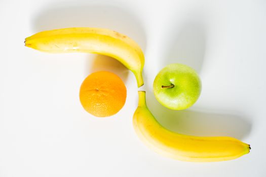 A whole granny smith apple, an orange and two bananas against a plain white background
