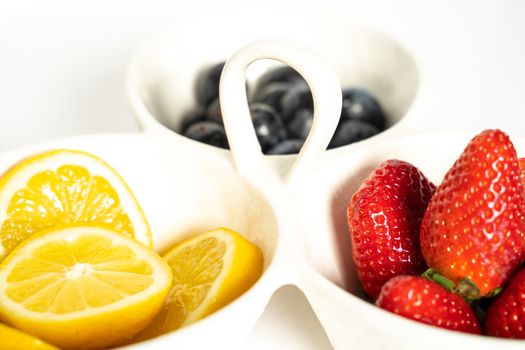 A serving dish filled with strawberries, lemon slices and black grapes against a plain white background