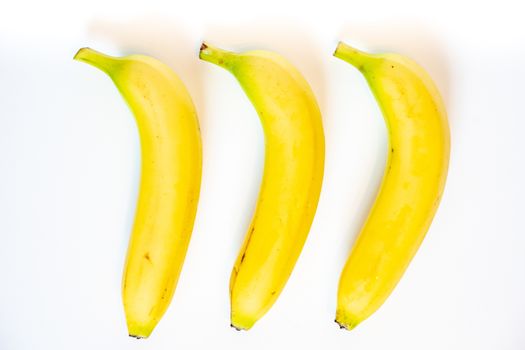 Three whole bananas laid in a row against a plain whit background
