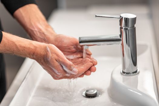 Washing hands man rinsing soap with running water at sink, Coronavirus prevention hand hygiene. Corona Virus pandemic protection by cleaning hands frequently.