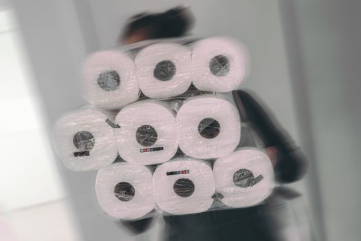 Coronavirus shopping frenzy at store woman carrying many packages of toilet paper in panic buying afraid of shortage in store. Motion blur.