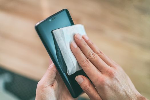 Cleaning mobile phone screen with disinfecting wet wipes for clean smartphone preventive wiping for COVID-19 Coronavirus outbreak contamination prevention.
