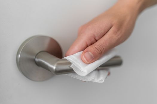 Coronavirus COVID-19 Prevention cleaning woman wiping doorknob with antibacterial disinfecting wipe for killing corona virus on surfaces or touching public bathroom handle with tissue.