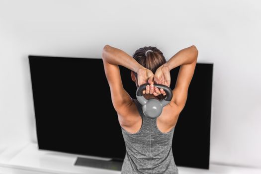 Home exercise strength training workout overhead triceps extension muscles exercises woman watching online tv fitness class live streaming at home. Gym girl lifting kettlebell weights.