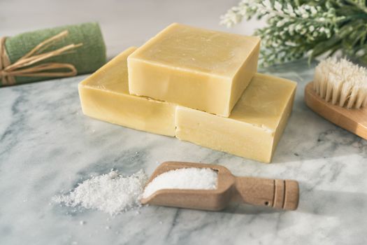 Handmade natural soap bars with epsom salt and scrubbing towel for skincare exfoliation spa therapy. Top view of olive oil soaps on marble background.