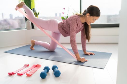 Resistance band fitness at home Asian woman doing leg workout donkey kick floor exercises with strap elastic. Glute muscle activation with kickback for thighs cellulite.