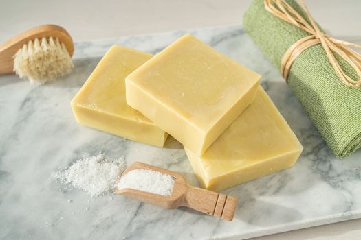 Natural soap homemade bars for exfoliation skincare with epsom salts and ramie towel scrubbing brush on marble top.