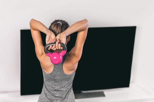 Home strength training workout overhead triceps extension muscles exercises woman watching online tv class live streaming at home. Fitness gym girl lifting kettlebell weights.
